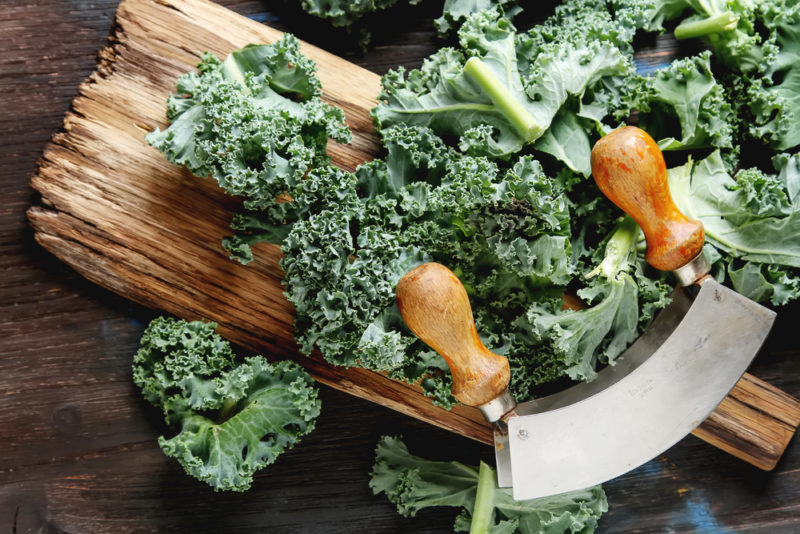 A wooden board with grains, with curly kale and a knife for chopping