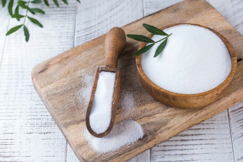 A wooden board with a bowl of erythritol and a scoop of erythritol