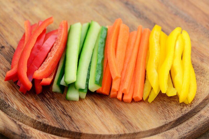 A circular wooden board with slices of yellow pepper, red pepper, cucumber, and carrots