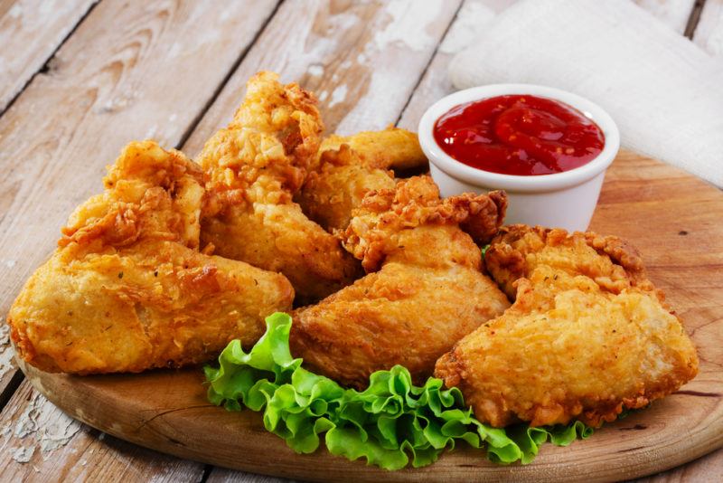 A wooden board with fried chicken and some dip on a wooden table or deck