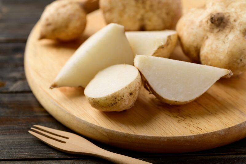 A wooden board with whole and partial pieces of jicama, next to a small wooden fork