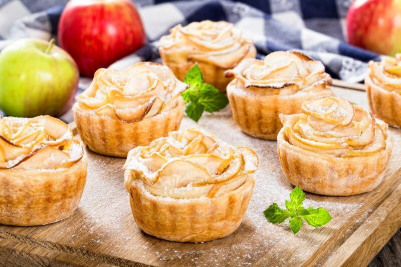 A wooden board with small apple pies and some apples in the background