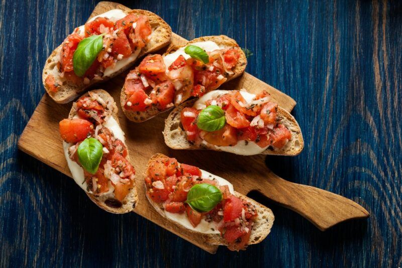 A wooden board with five pieces of Italian bruschetta on a blue table