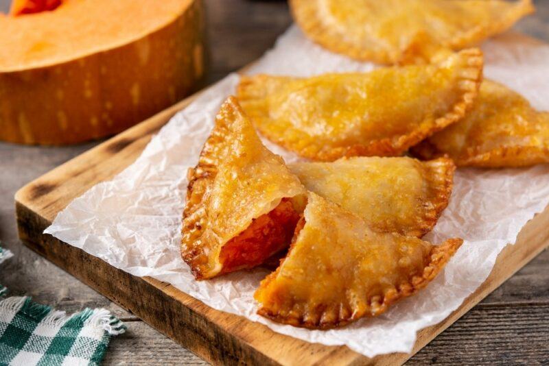 A wooden board with parchment paper and a couple of pumpkin empanadas