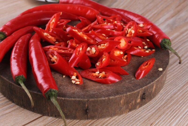 A wooden board with red jalapenos and some that have been sliced