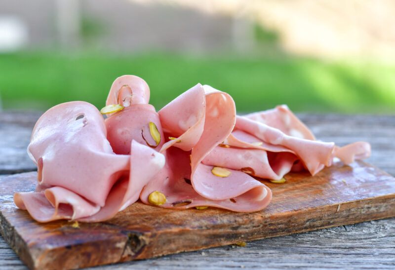 A wooden board on a table outside with many shaved pieces of bologna