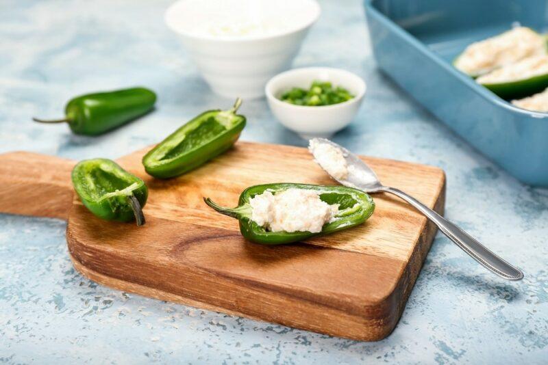 A wooden board with sliced green jalapenos that are being used to make jalapeno poppers