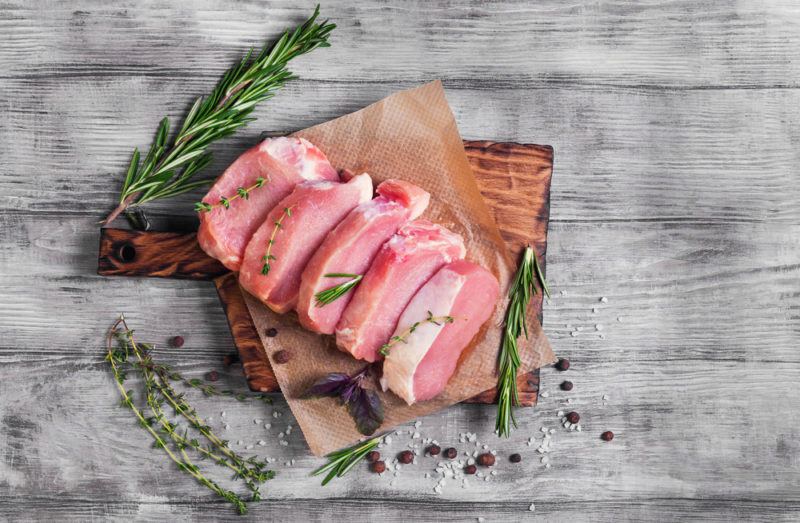 Sliced pork with greenery on a wooden board on a table