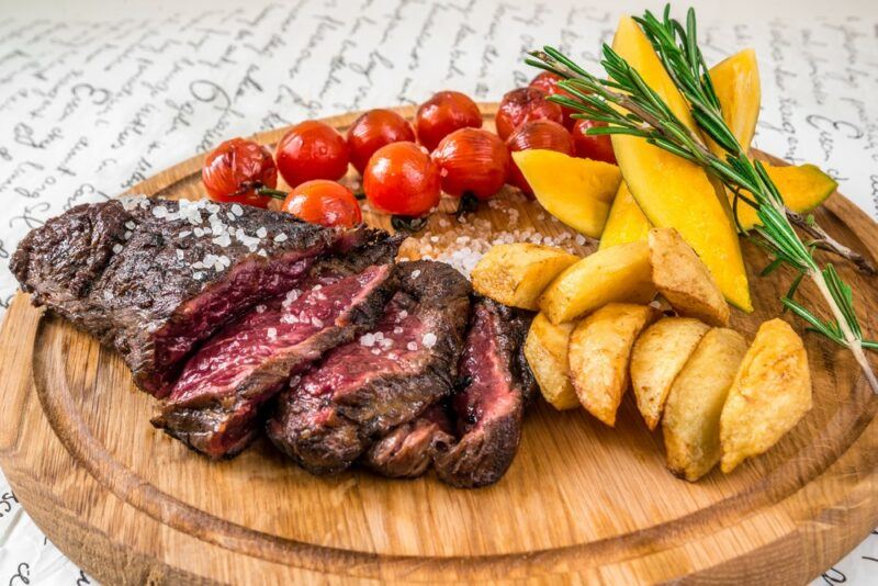 A wooden board with sliced steak, tomatoes, and potatoes