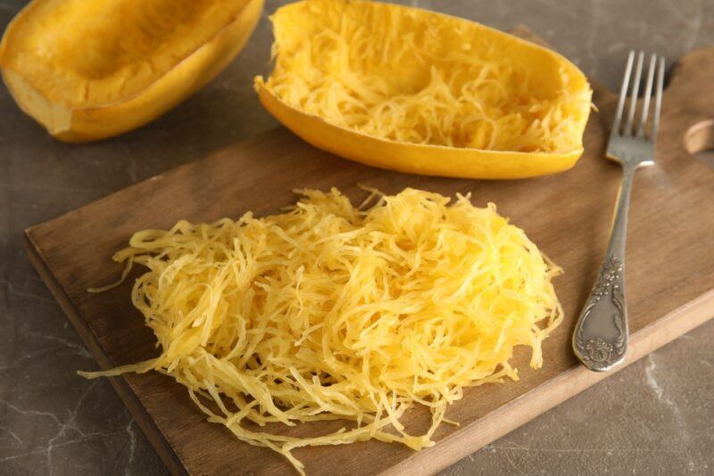 A wooden board with spaghetti squash strands, next to two emptied spaghetti squash halves