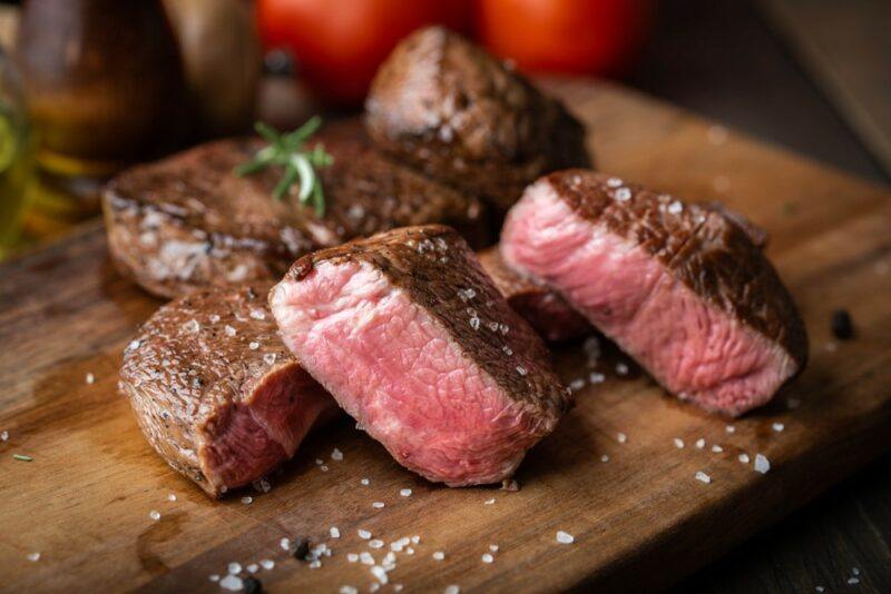 A wooden board with a tenderloin steak that's been cut into pieces, with salt scattered on the board