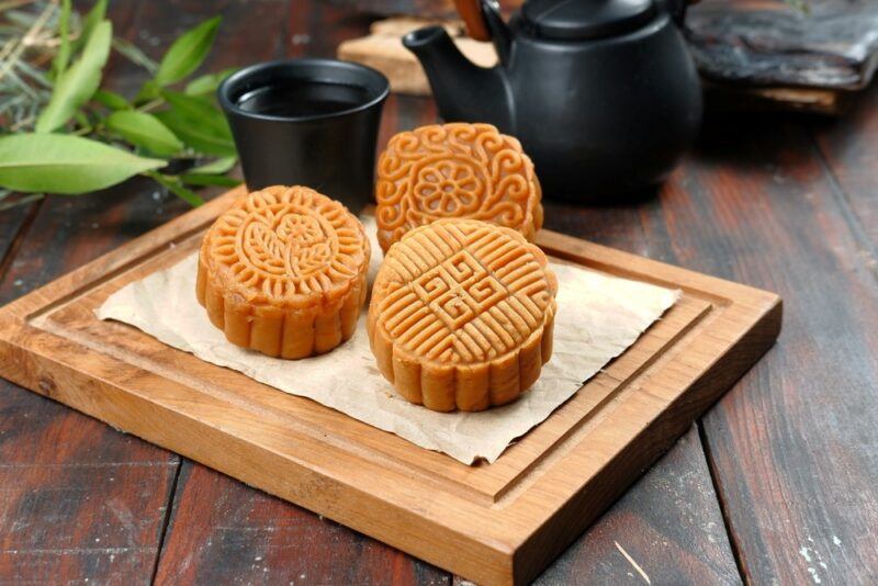 A wooden board with three mooncakes, in front of a black teapot and a black cup