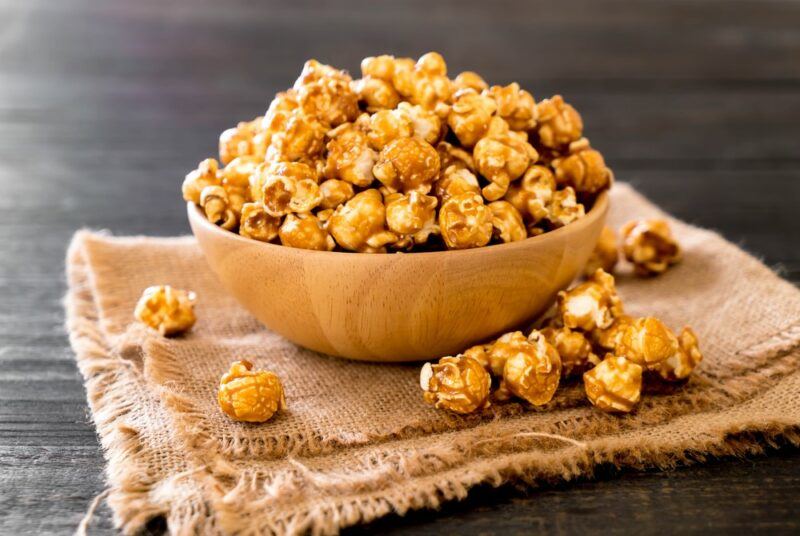 A wooden bowl containing caramelized ginger and lemongrass popcorn on a piece of cloth