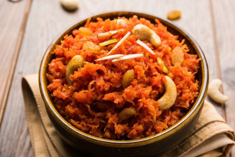 A brown bowl containing gajar ka halwa, on a piece of cloth, on a wooden table