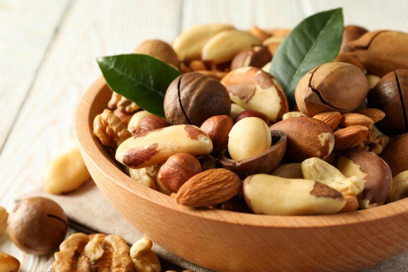 A wooden bowl containing a selection of nuts on a white table