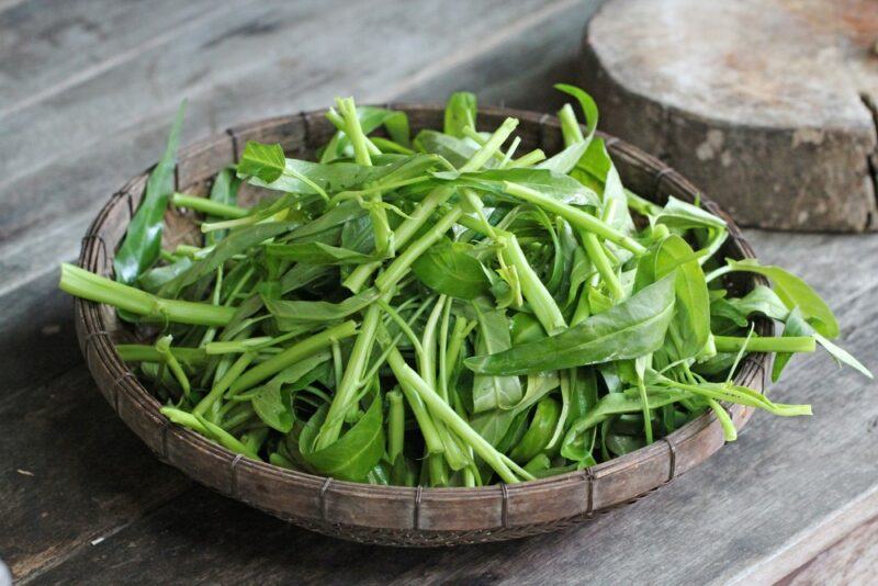 A brown wooden bowl containing water spinach leaves.