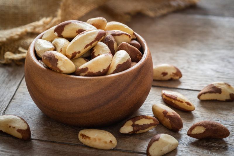 A small brown wooden bowl with Brazil nuts and more brazil nuts on the boards