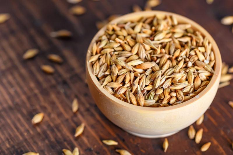 A small wooden bowl of barley with more spilling out onto the table