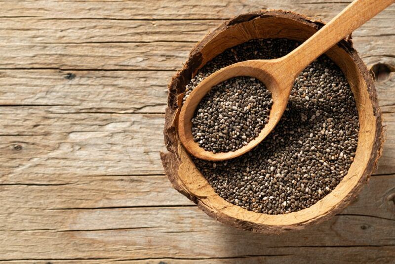 A small wooden bowl of chia seeds, with a wooden spoon on top