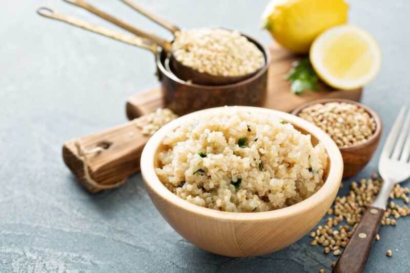 A wooden bowl containing cooked quinoa, with a smaller bowl and spoon containing more quinoa, along with a lemon and a lemon half