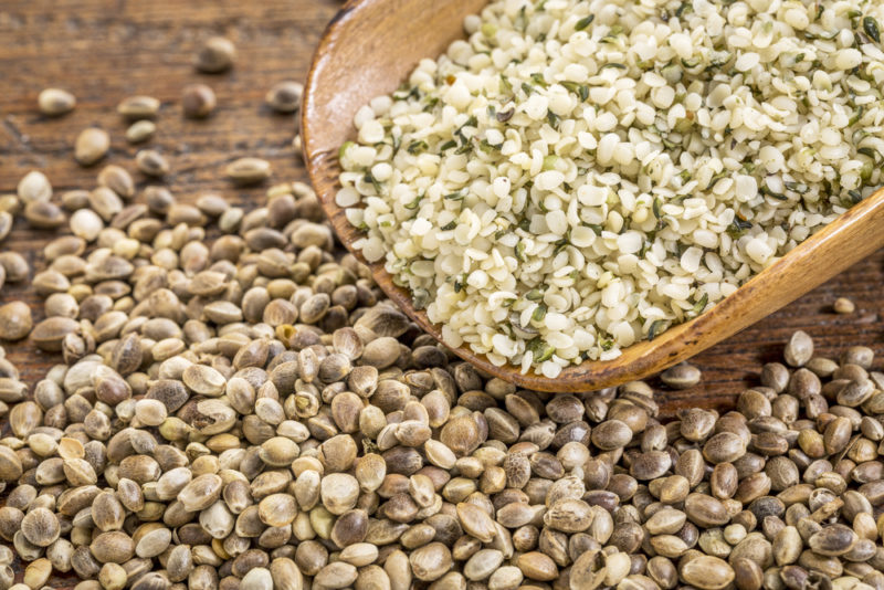 A bowl of hemp hearts next to hemp seeds scattered on a table