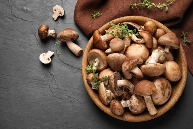 A brown plate or bowl with fresh foraged mushrooms, and a few mushrooms scattered on the black table