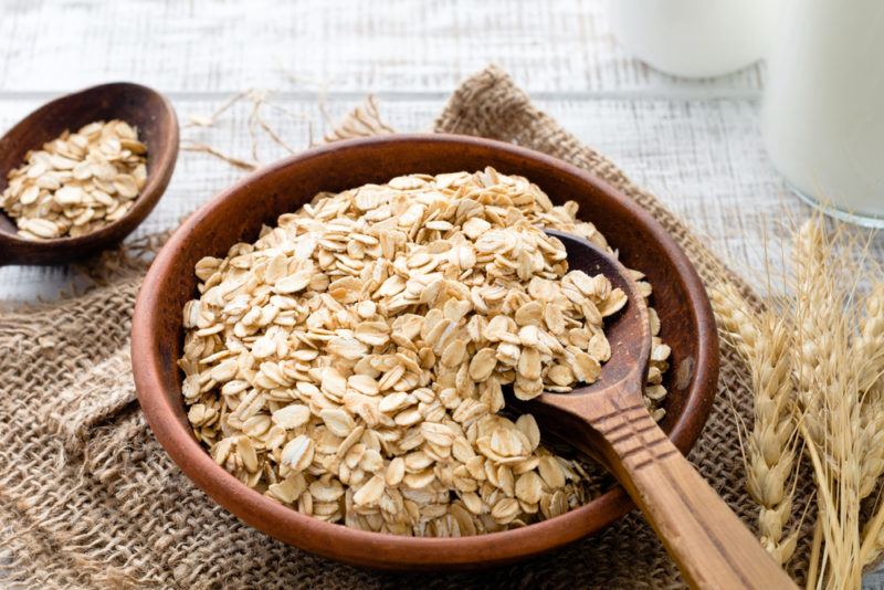 A wooden bowl of oatmeal on a brown cloth, with a spoon of oatmeal in the bowl and another on the table