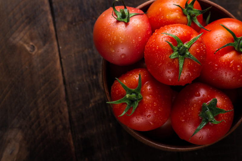 A wooden bowl of fresh red tomatoes on a wooden table