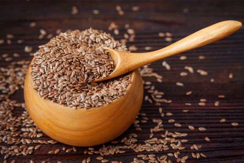 A brown bowl that contains flax seeds and a spoon