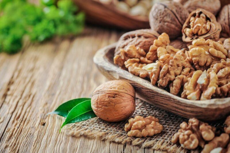 A wooden bowl with walnuts, next to a single walnut on the table