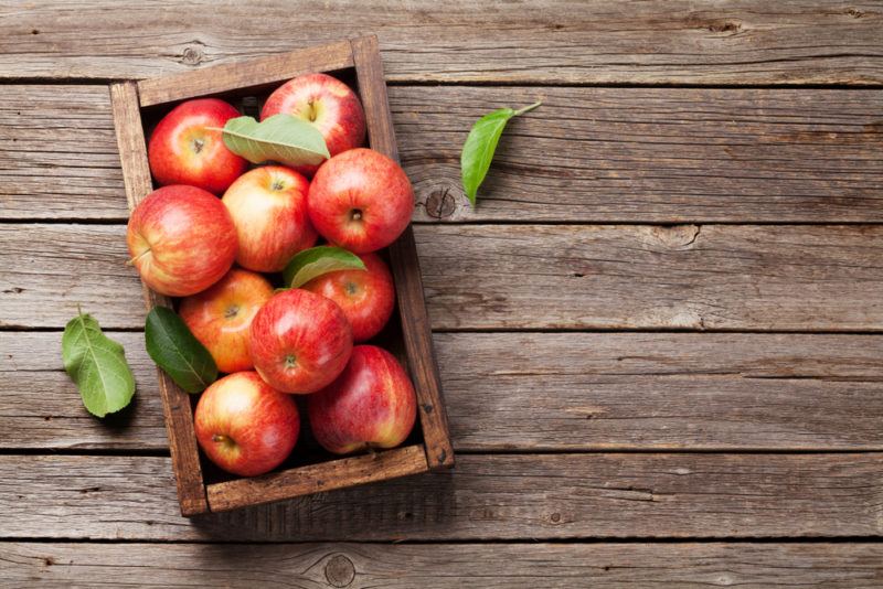 A wooden box that contains fresh apples on a wooden deck