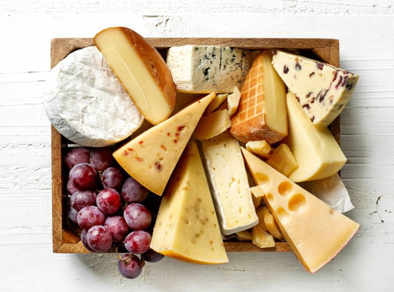 A wooden box filled with a selection of cheeses and some grapes