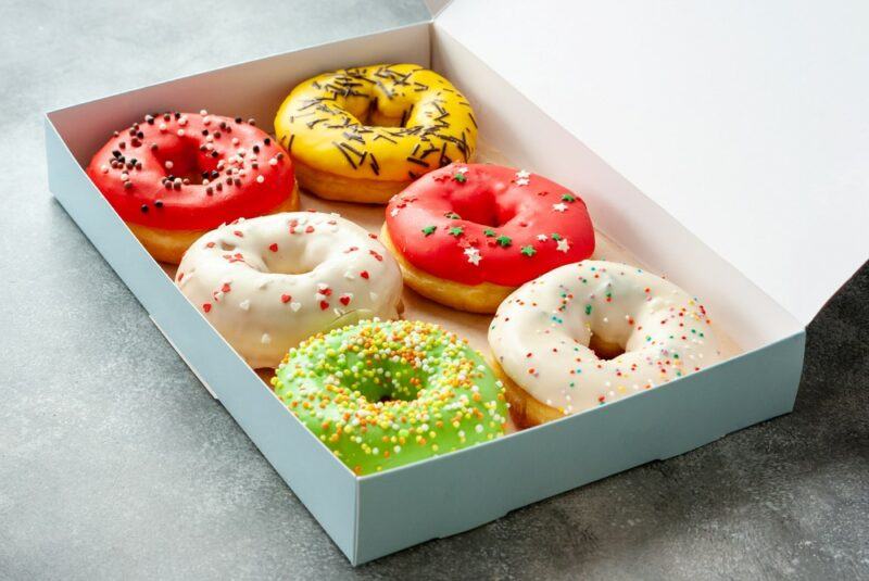 A wooden box containing six types of brightly colored donuts with sprinkles