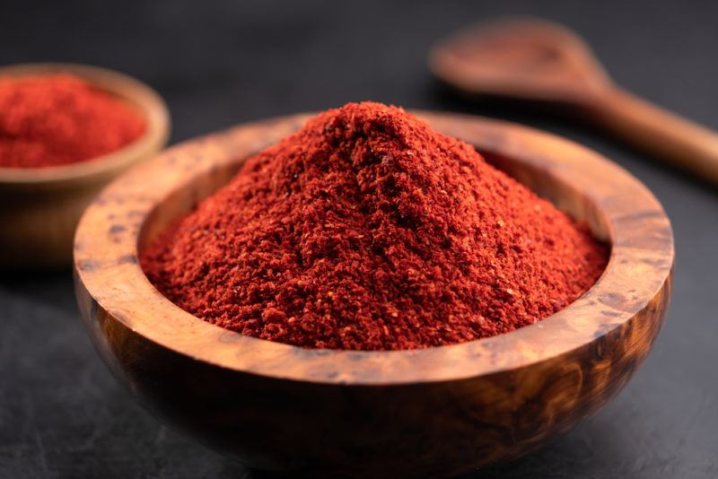 A wooden bowl of paprika with a spoon and a second dish in the background