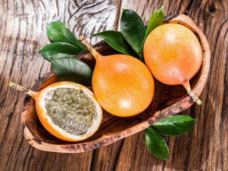 A wooden table with a dish containing two whole granadilla fruits, plus one half