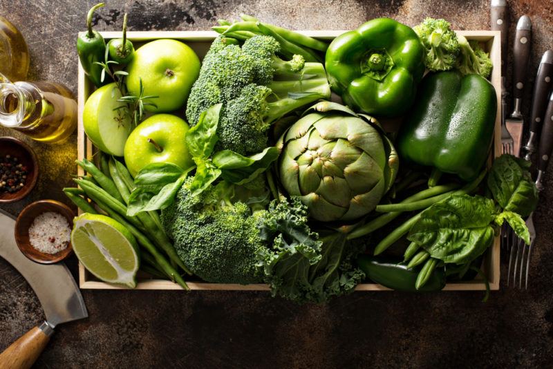 A wooden crate filled with many types of green vegetables and a few green fruits