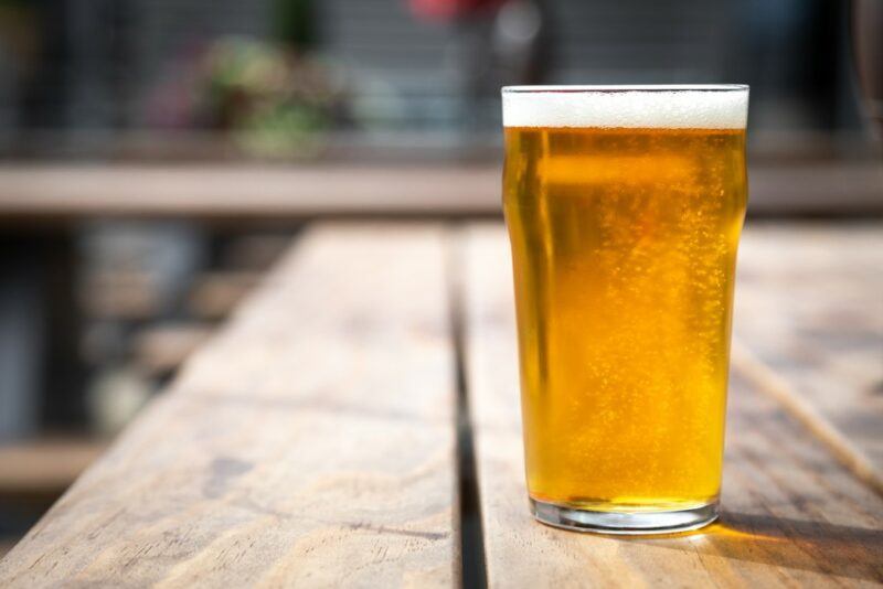 A wooden table or deck with a single large glass of pilsner