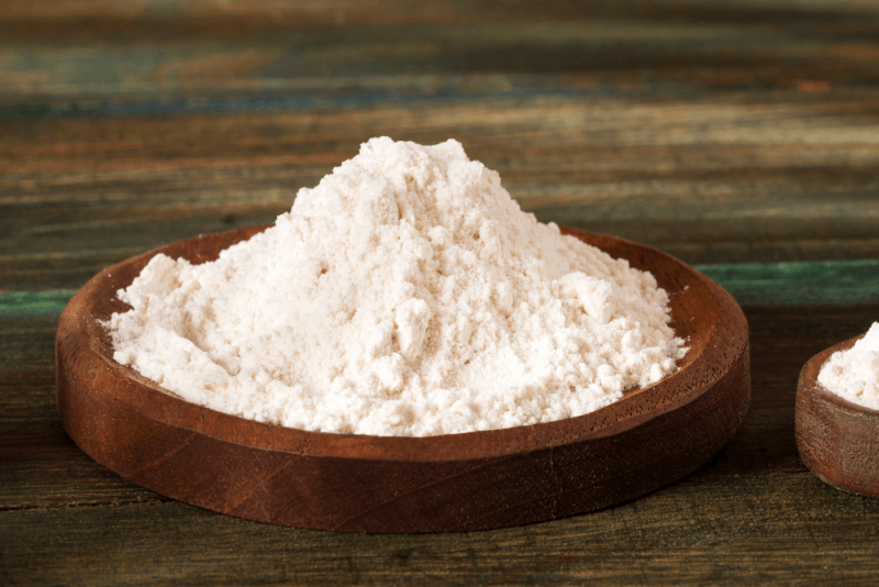 A wooden table with a small brown dish of tapioca flour.