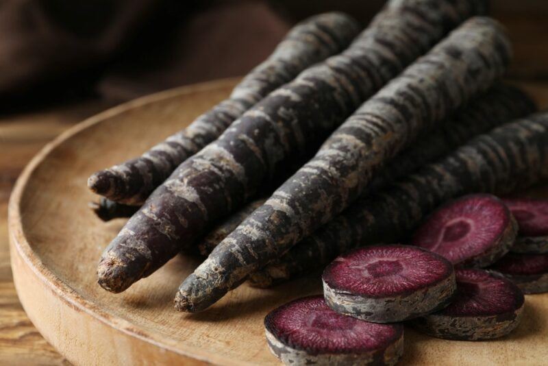 A wooden board with a collection of black carrots, including a few black carrot slices