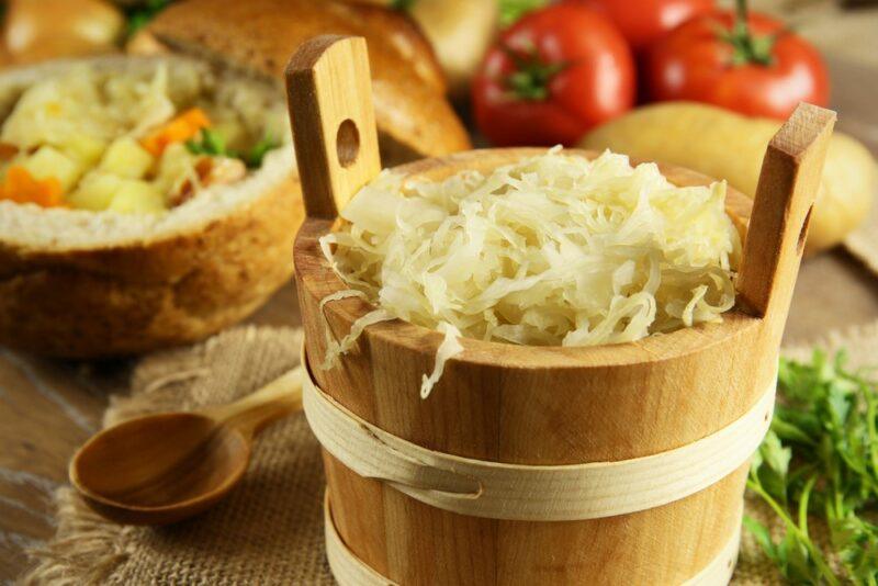 A large pail of sauerkraut with some ingredients in the background