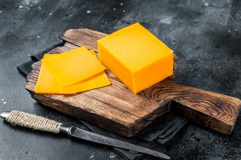 A wooden board with a large block of bright orange cheese and some slices