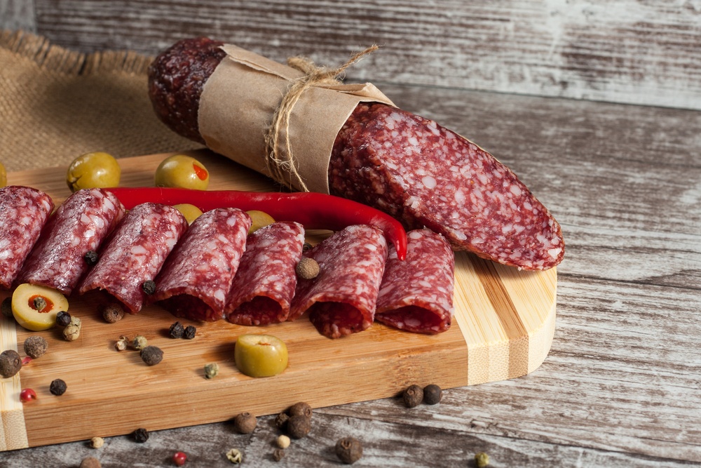 A wooden board with a whole salami and sliced salami