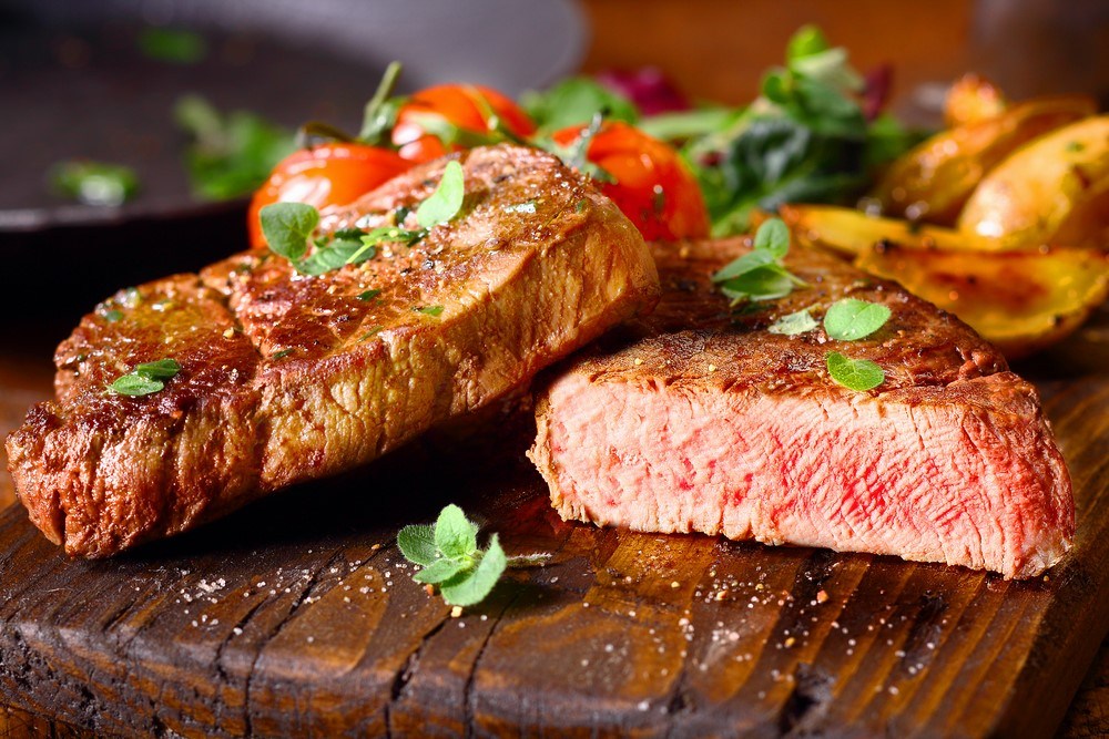 Two pieces of lean steak on a wooden board. One has been cut in half.