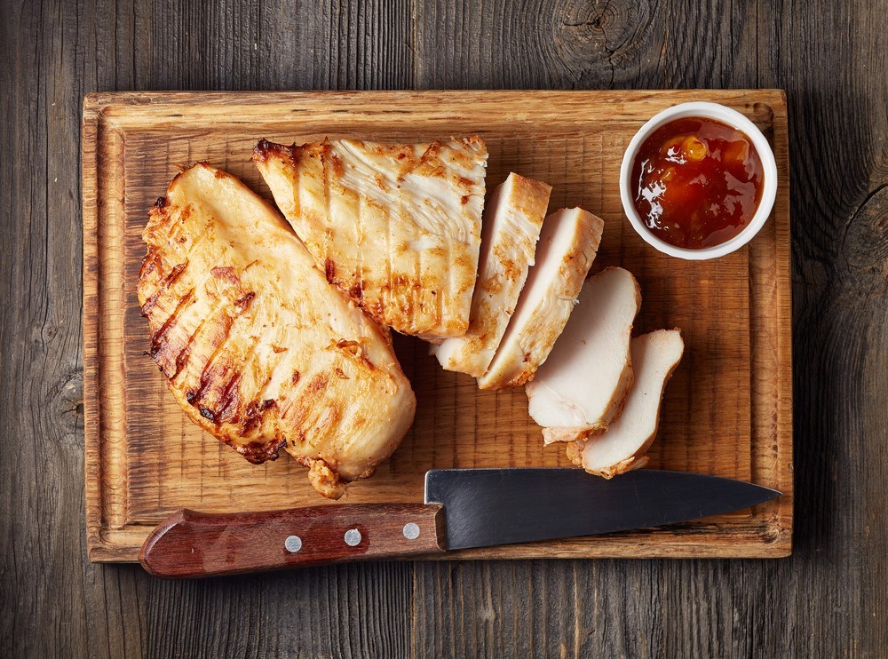 A wooden board with two chicken breasts, one of which has been sliced