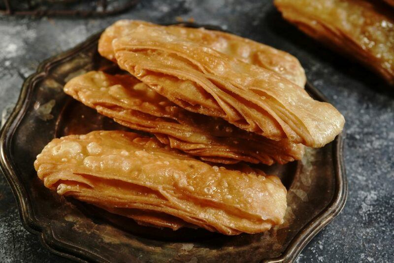 A dark plate containing four pieces of a layered dessert called khaja