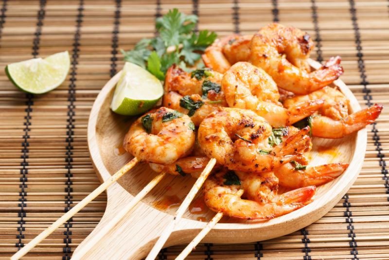 A wooden ladel with cooked shrimp on skewers