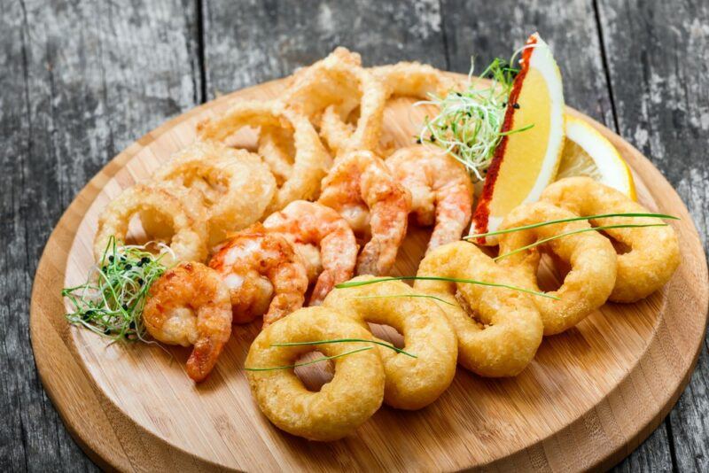 A wooden board with cooked seafood and onion rings