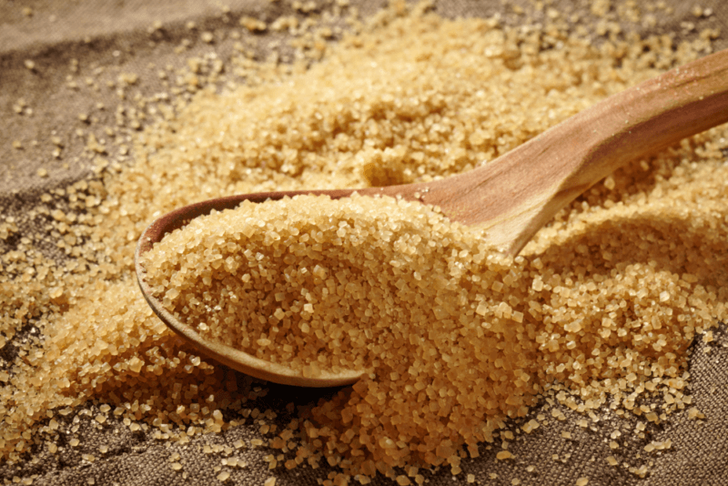 A pile of brown sugar on a table, with a wooden spoon and even more brown sugar.