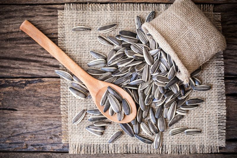 A bag of sunflower seeds spilling out onto a table next to a wooden spoon