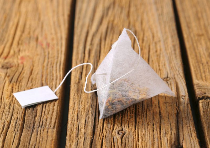 A pyramid-shaped teabag with herbs on a wooden table